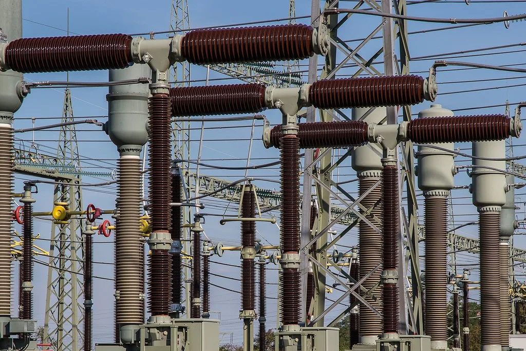 A row of dark porcelain bushings on outdoor substation equipment