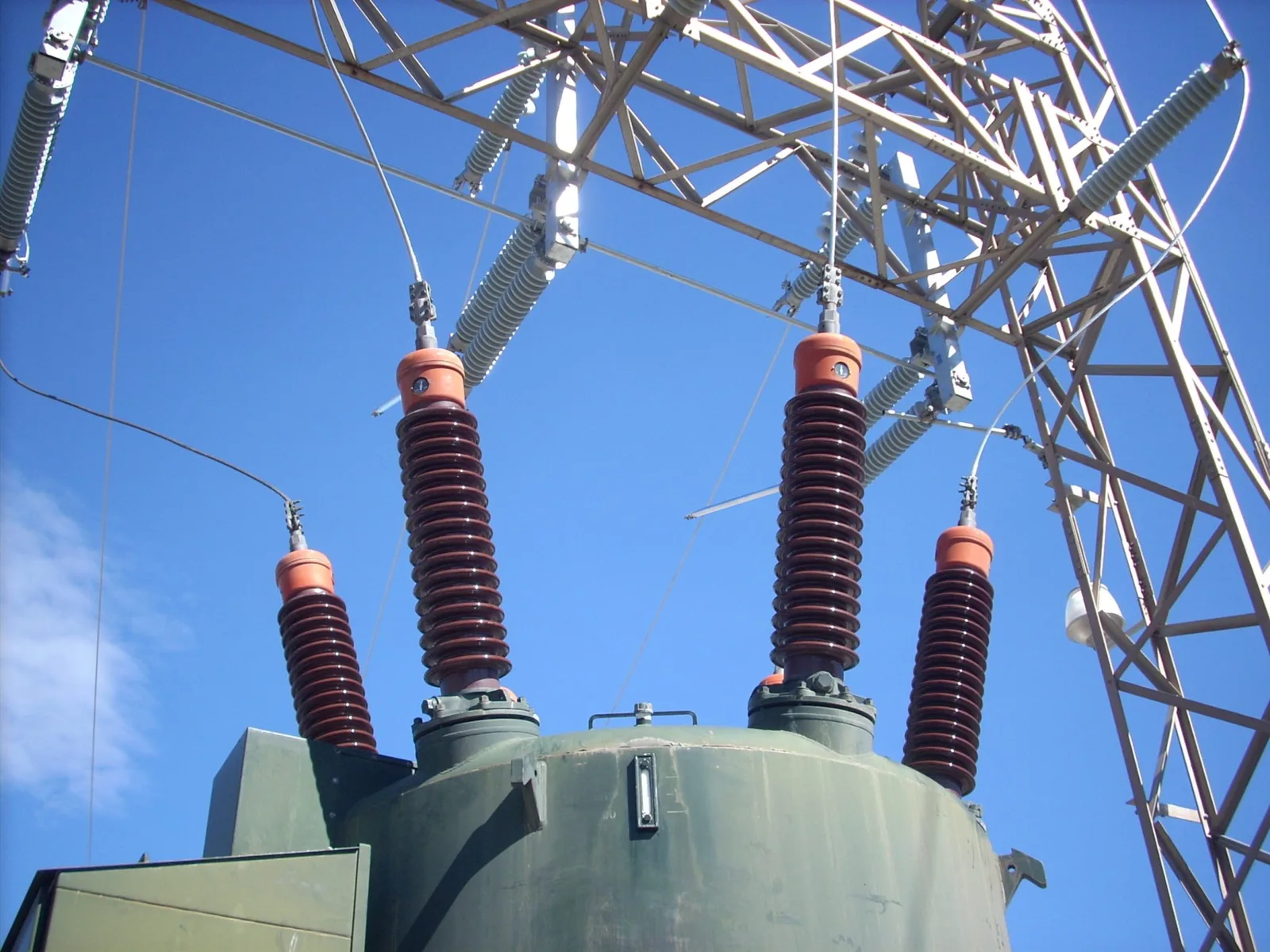 Four porcelain bushings on top of a large oil-filled transformer at a substation